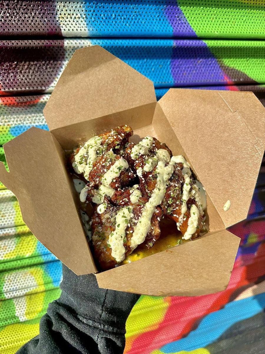 Saucy chicken wings in a takeaway box in front of a colourful street mural
