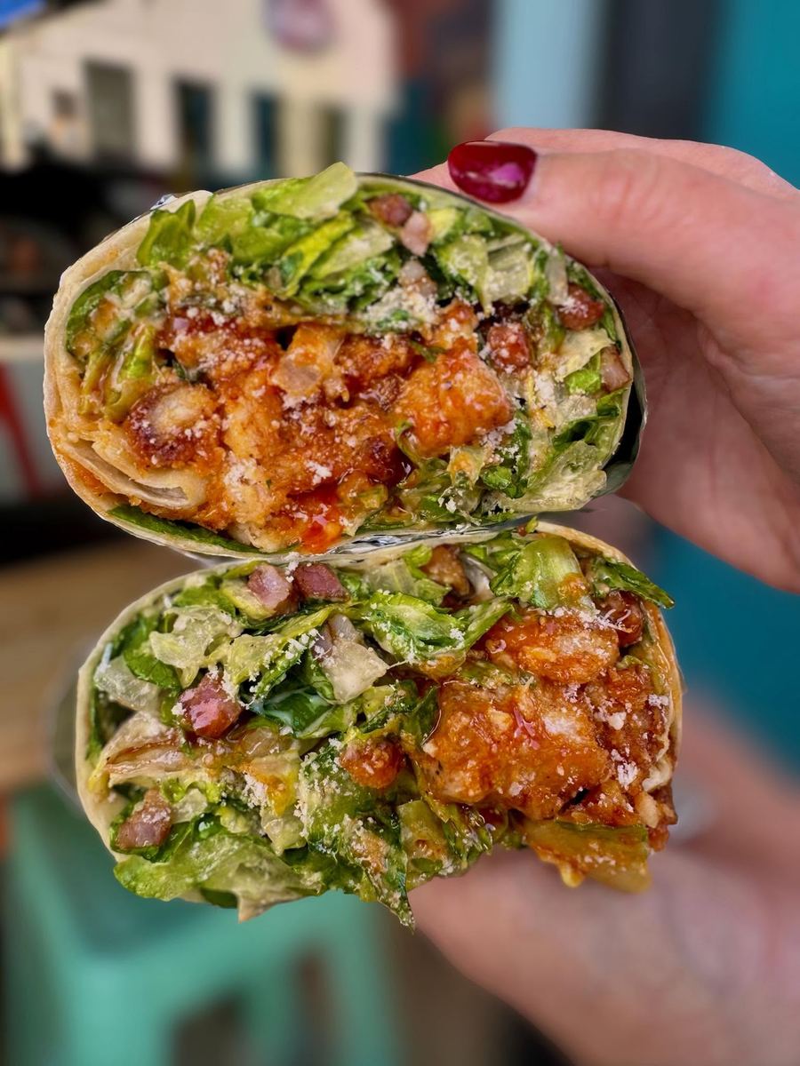 A crispy buffalo chicken wrap cut in half and held up outside Guapo