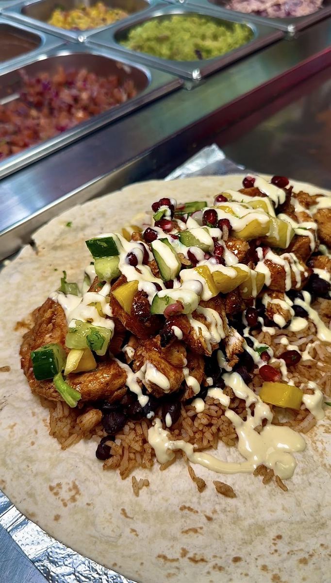 A Guapo burrito being filled with rice, beans, chicken, salsa, and sauce