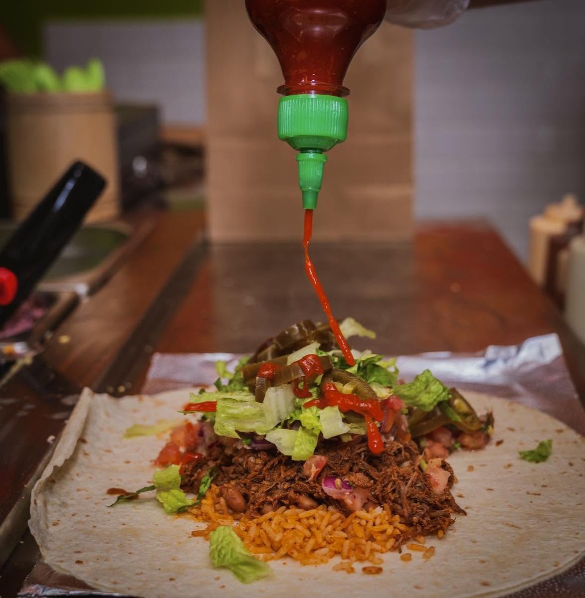 Hot sauce being poured over a burrito filling on a tortilla